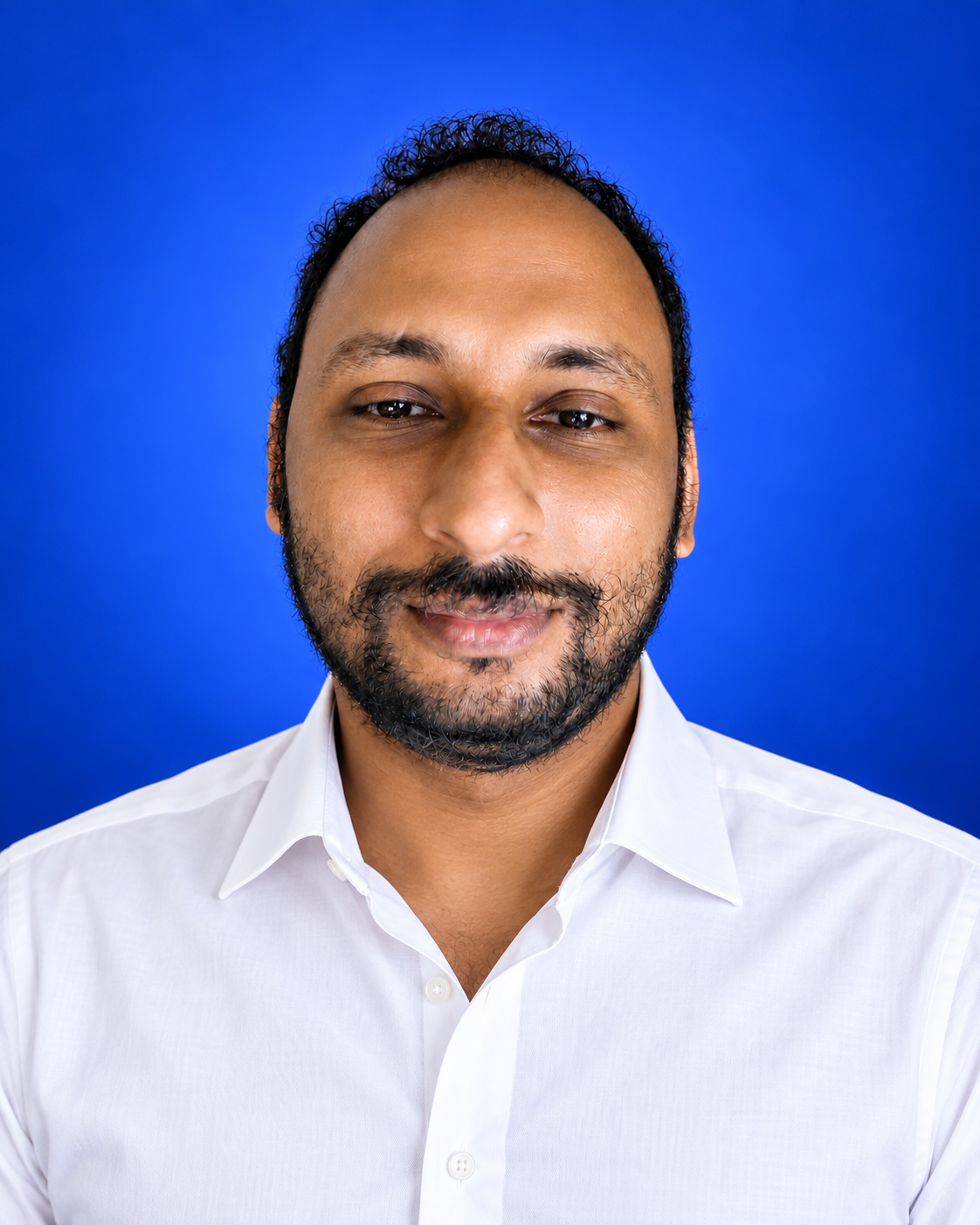 Jins Mathew in a white formal shirt, photographed against a studio backdrop